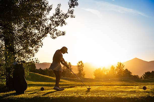 Woman golfer in silhouette swinging a golf club on a golden course at sunset.