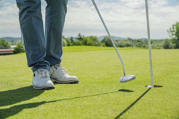 Golfer putting with golf clubs on green grass.
