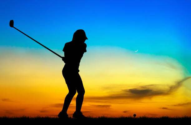 Silhouette of a golfer ready to swing a golf club against a stunning sunset sky.