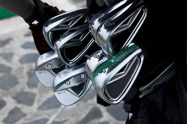 Close-up of shiny silver golf club heads in a dark golf bag.