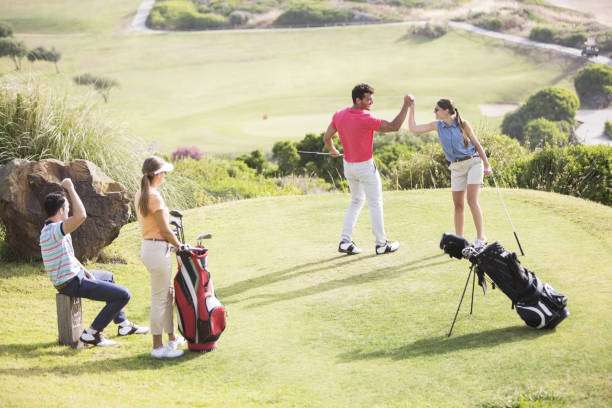 Golfers celebrate on the course; two others stand by a golf club bag.