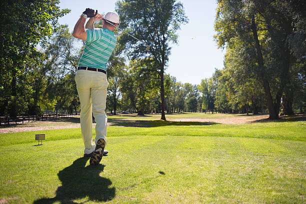 Golfer swinging golf clubs on a sunny green course.