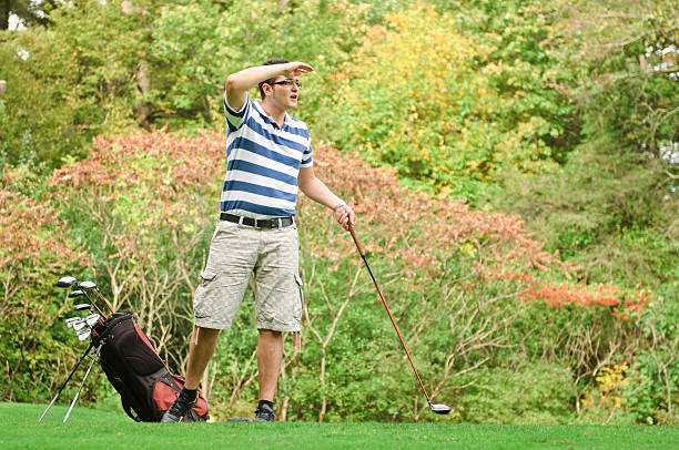 Man on a golf course searching for his ball with a golf club beside him.