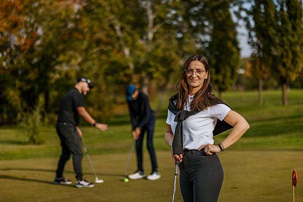 Smiling woman on a golf course with other players and their golf clubs in background.