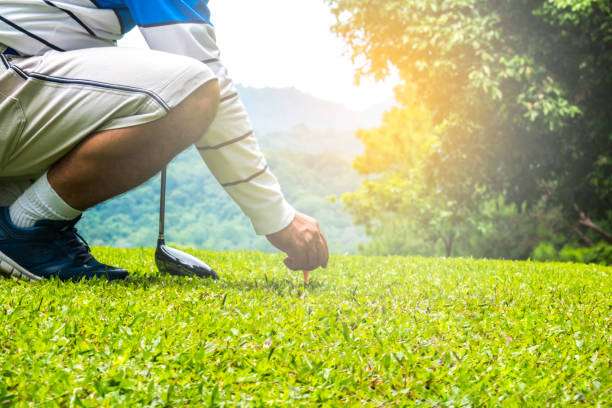 Golfer placing golf ball on tee with golf clubs nearby.
