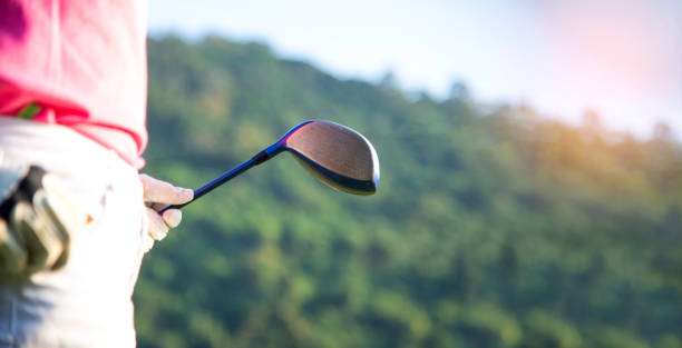 Close-up of a golfer holding a driver golf club with scenic mountains in background.