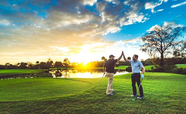 Two joyful golfers high-fiving on a scenic golf club course at sunset.
