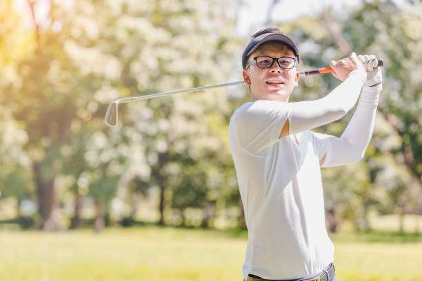 Young man in a cap mid-swing with a golf club on a sunny course.